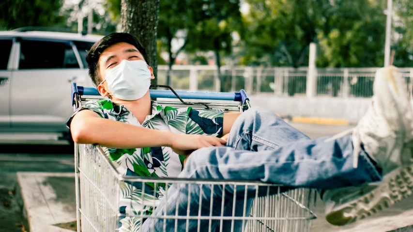 a man sitting in a shopping cart wearing a face mask, by Julia Pishtar, pexels, realism, resting, teenage boy, yee chong, worksafe. instagram photo