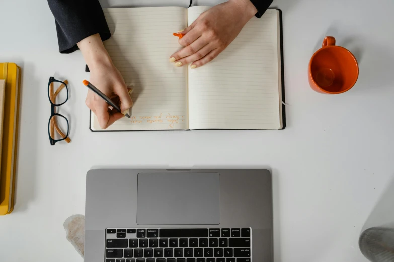 a person writing in a notebook next to a laptop, trending on pexels, flat lay, background image, professional image, 1 2 9 7