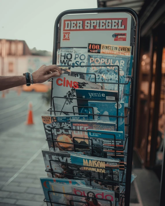 a man standing next to a sign with magazines on it, by Kristian Zahrtmann, pexels contest winner, happening, kreuzberg, gif, jukebox, 🚿🗝📝