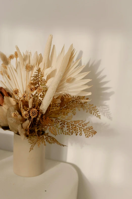 a vase with a bunch of dried flowers in it, by Jessie Algie, beige and gold tones, soft white glow, dried palmtrees, she has a crown of dried flowers