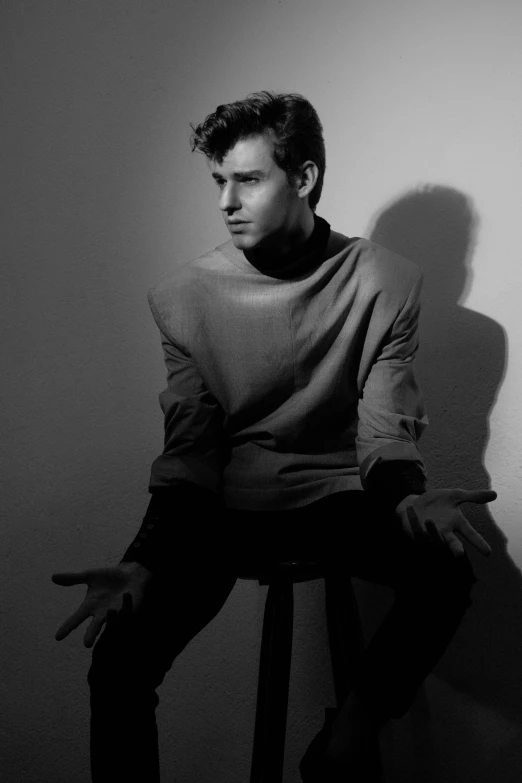 a black and white photo of a man sitting on a stool, inspired by Harry Morley, unsplash, photorealism, flume cover art, handsome prince, nathan fielder, portrait of chris evans