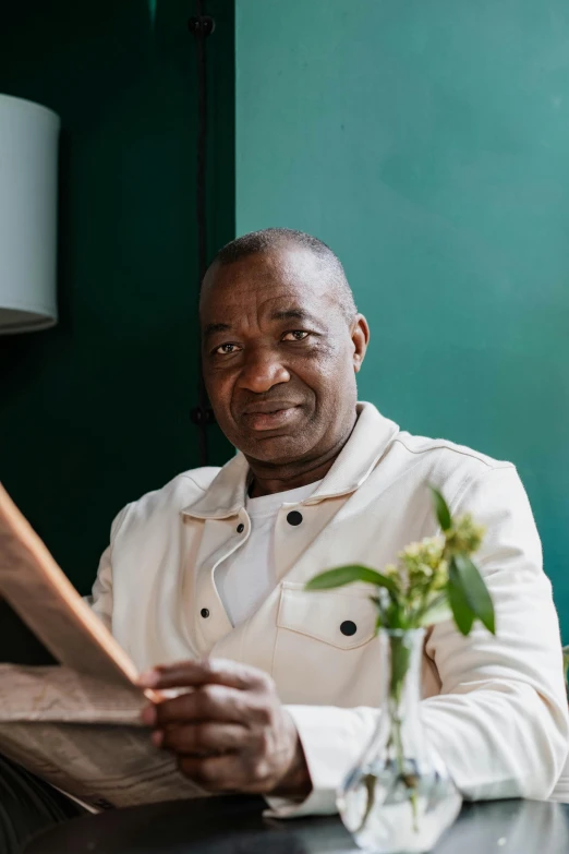 a man sitting at a table reading a newspaper, an album cover, inspired by Barthélemy Menn, pexels contest winner, in a dark green polo shirt, happy chef, he is about 60 years old, alphonse musha