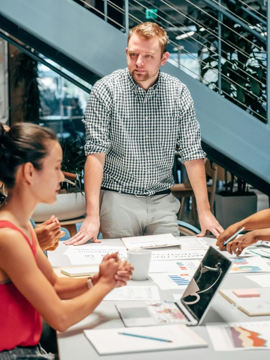 a group of people sitting around a table, a picture, wearing business casual dress, profile image, multiple stories, man standing