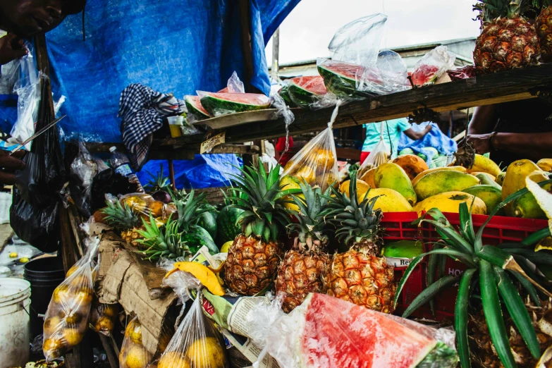 a man standing in front of a fruit stand, by Daniel Lieske, unsplash, samoan features, plastic waste, square, pineapples