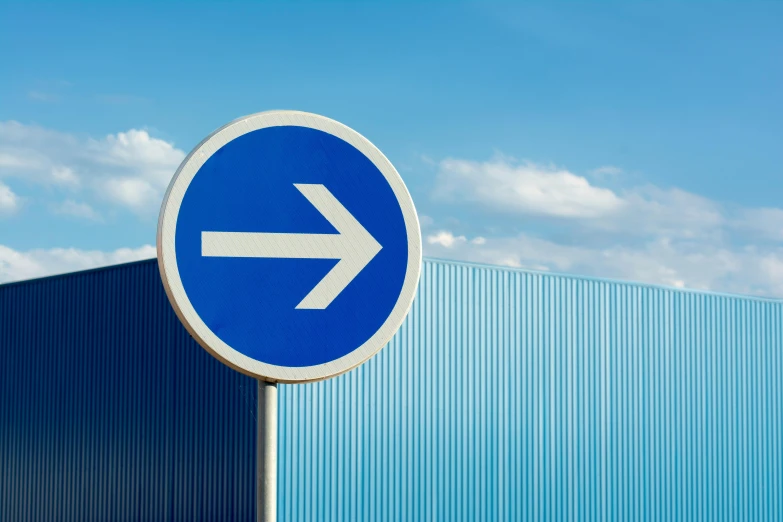 a blue and white arrow sign in front of a building, by Paul Bird, postminimalism, warehouses, crossing the blue horizon, contain, very round