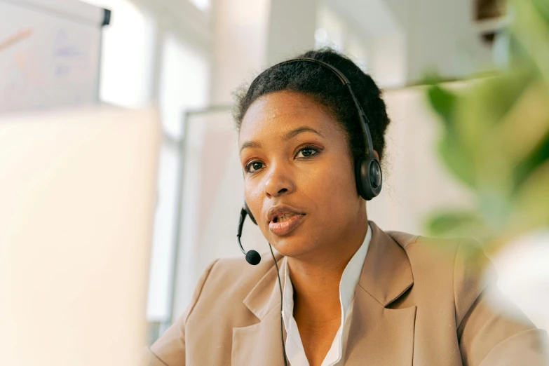 a woman sitting in front of a computer wearing a headset, trending on pexels, hurufiyya, mongezi ncaphayi, avatar image, brown, detailed professional photo