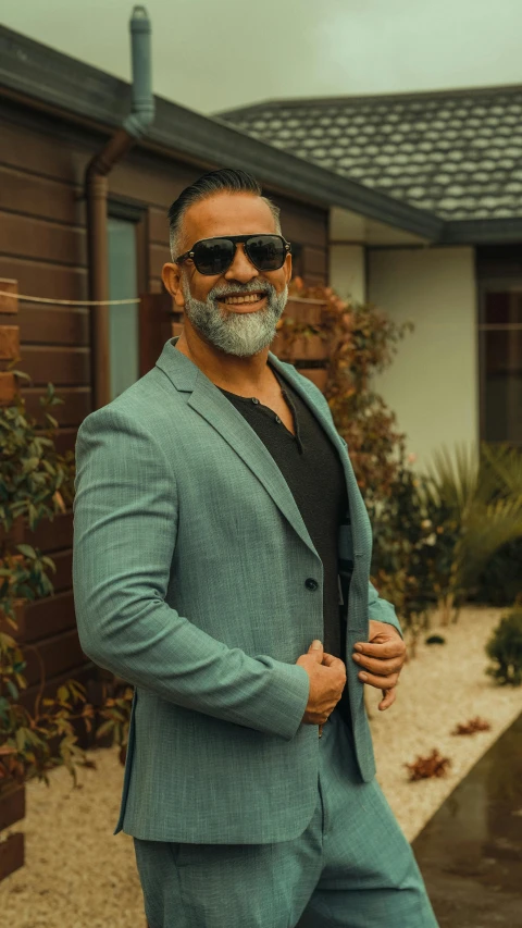 a man in a suit and sunglasses standing in front of a house, by Alexander Fedosav, pexels contest winner, grey trimmed beard, macho pose, kyza saleem, smiling male