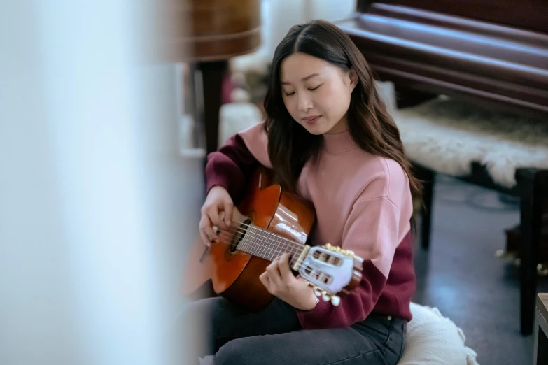 a woman sitting on the floor playing a guitar, inspired by Song Xu, pexels contest winner, sweater, pictured from the shoulders up, gemma chan, pokimane