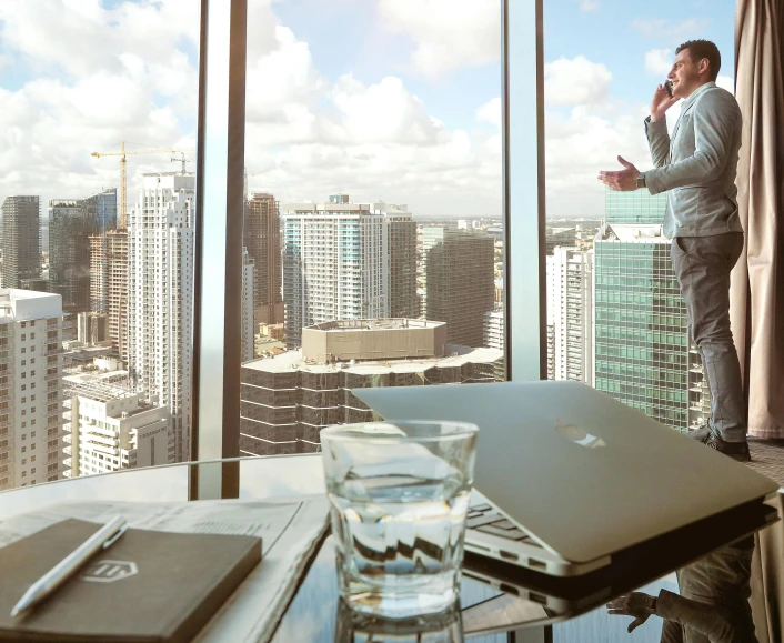 a man standing in front of a window talking on a cell phone, pexels contest winner, happening, auckland sky tower, sitting at a computer desk, corporate holograms, top floor boss shit