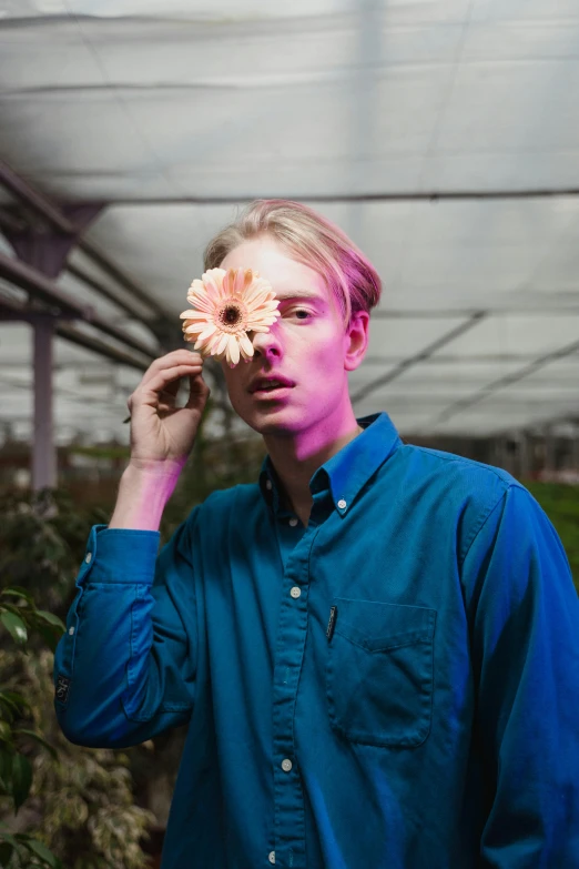 a man holding a flower in front of his face, an album cover, unsplash, aestheticism, blonde british man, greenhouse, attractive androgynous humanoid, lights with bloom