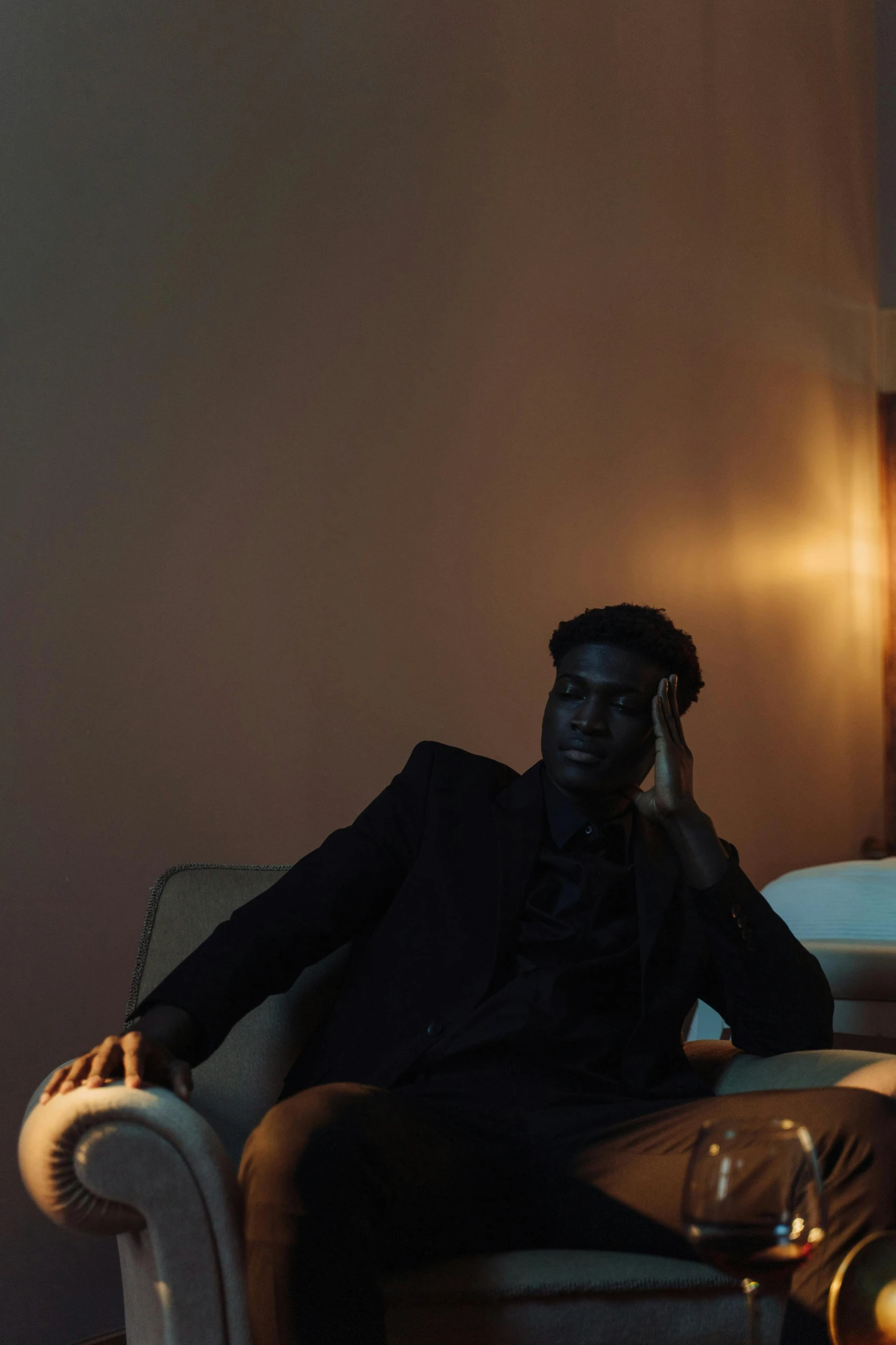a man sitting on a couch talking on a cell phone, an album cover, by Elsa Bleda, pexels contest winner, dark black skin, elegant pose, sitting in bedroom, male with halo