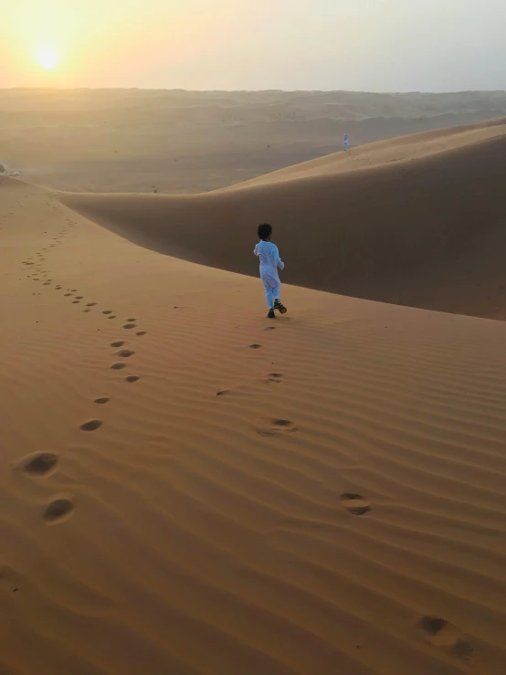 a person walking on a sand dune in the desert, in the middle of the desert, in the evening