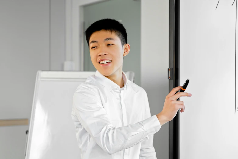 a man standing in front of a whiteboard holding a cell phone, a picture, inspired by Tooth Wu, pexels contest winner, wearing a light shirt, doing an elegant pose, 1 6 years old, side portrait imagery