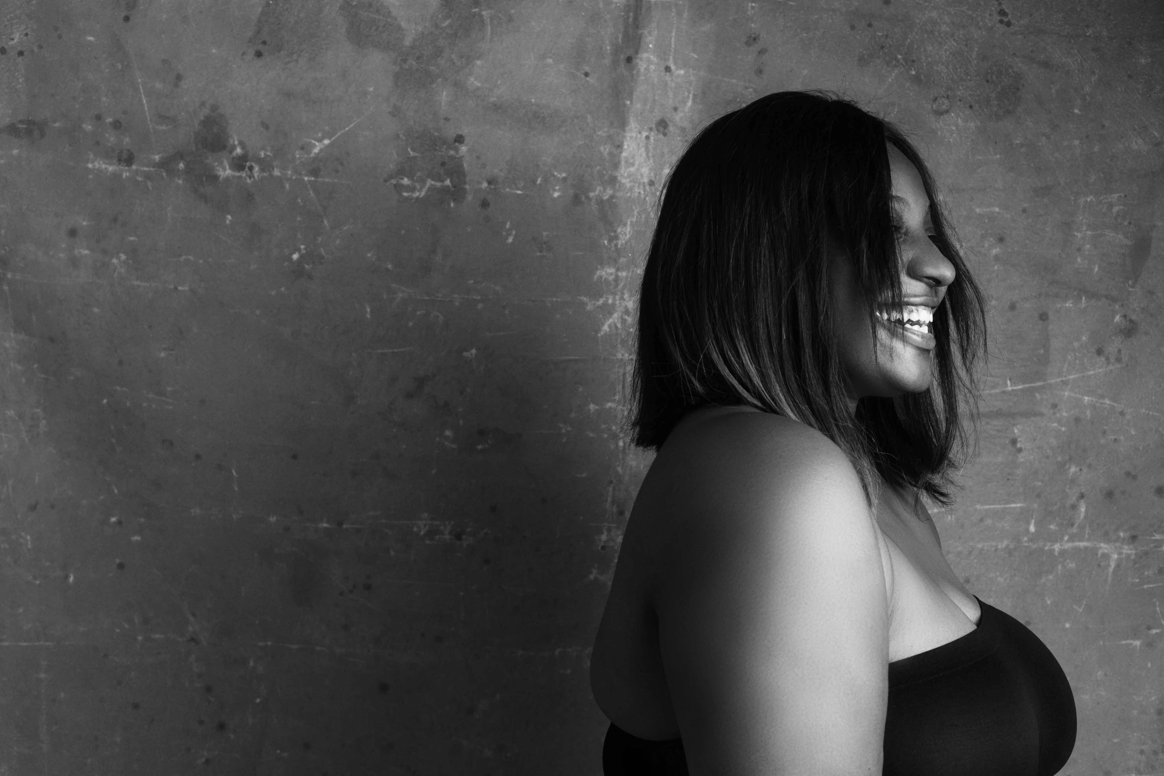 a black and white photo of a woman in a bra, a black and white photo, unsplash, mutahar laughing, curved. studio lighting, dayanita singh, leaning against the wall