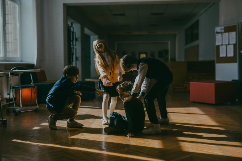 a group of people standing on top of a hard wood floor, by Emma Andijewska, pexels contest winner, kids playing, bullying, kneeling, back - lit