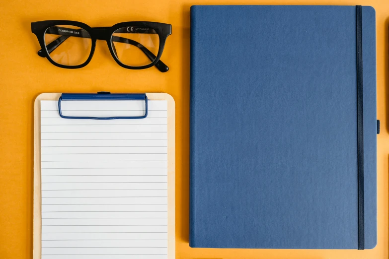 a notebook, pen and glasses on a yellow background, by Carey Morris, pexels, dark blue + dark orange, square rimmed glasses, background image, clipboard