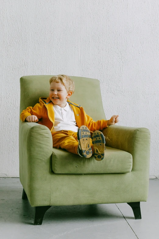 a little boy sitting on top of a green chair, pexels, yellow clothes, happy toes, relaxing on a modern couch, laughing