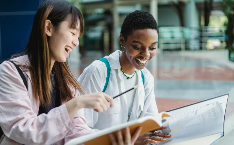 a couple of women sitting next to each other on a table, pexels contest winner, academic art, read a directory book, varying ethnicities, very excited, student