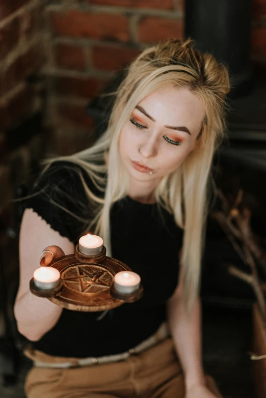 a woman holding two candles in front of a cake, inspired by Anne Stokes, trending on pexels, gothic art, on a wooden tray, portrait of kim petras, pentagrams, profile picture