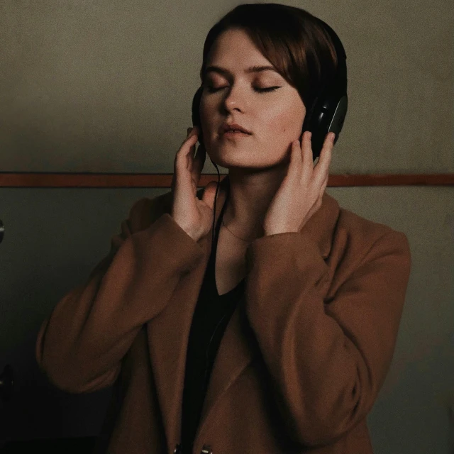 a woman in a brown coat talking on a cell phone, an album cover, pexels, bauhaus, with head phones, quiet beauty, clara oswald, indoor scene