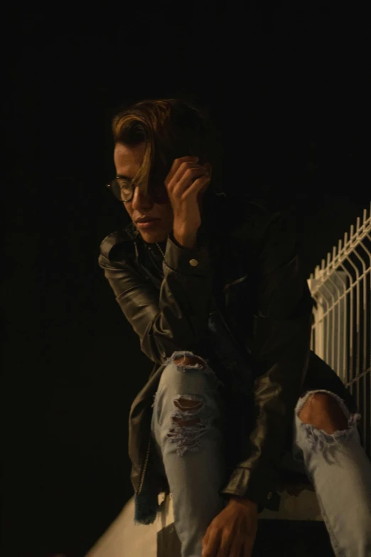 a woman sitting on a ledge talking on a cell phone, a picture, trending on pexels, antipodeans, dramatic dark lighting, still from a music video, androgynous male, standing astride a gate