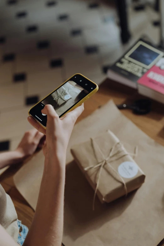 a woman sitting at a table taking a picture of a present, inspect in inventory image, brown, trending photo, cinematic shot ar 9:16 -n 6 -g