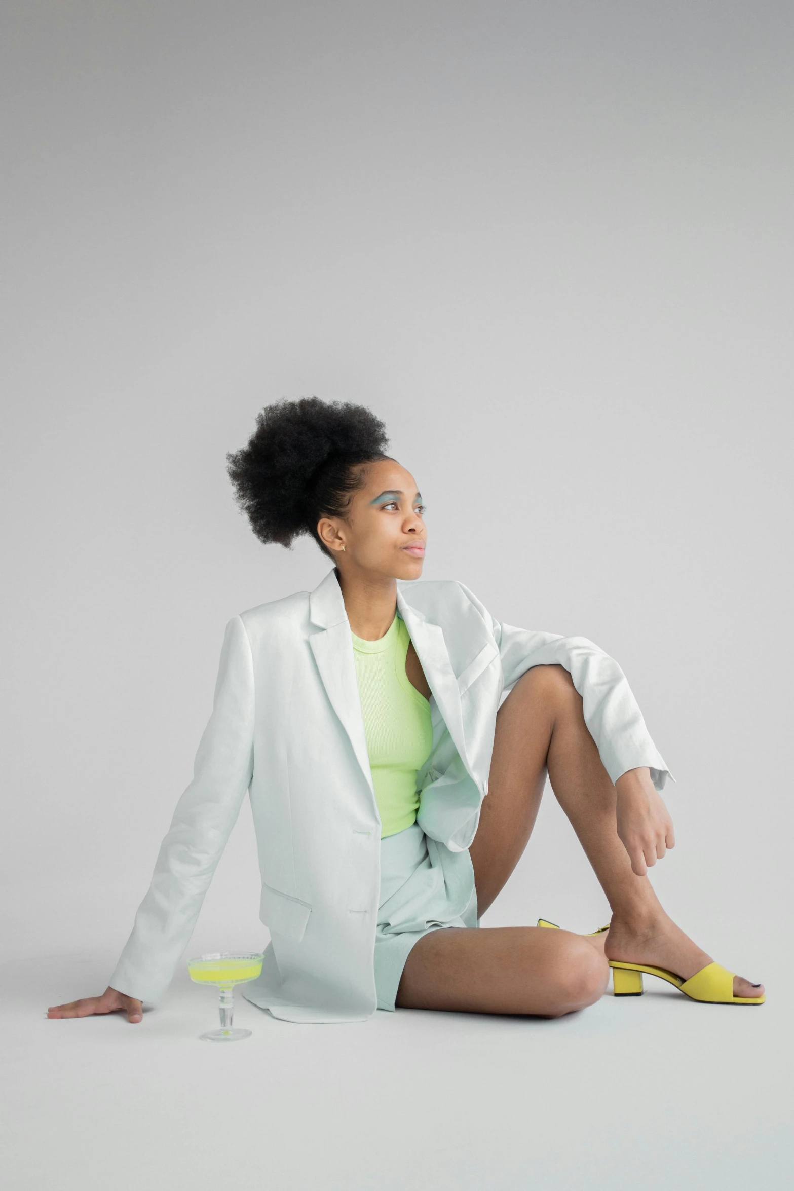 a woman sitting on the ground with her legs crossed, by Lily Delissa Joseph, neon colored suit, on a white table, wearing a light blue suit, wearing a neon green dress