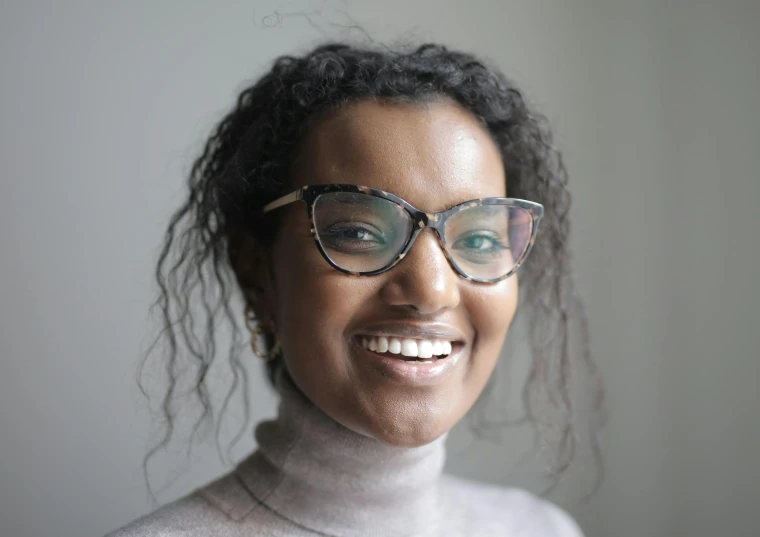 a close up of a person wearing glasses, inspired by Afewerk Tekle, smiling young woman, square rimmed glasses, mid length portrait photograph, brown