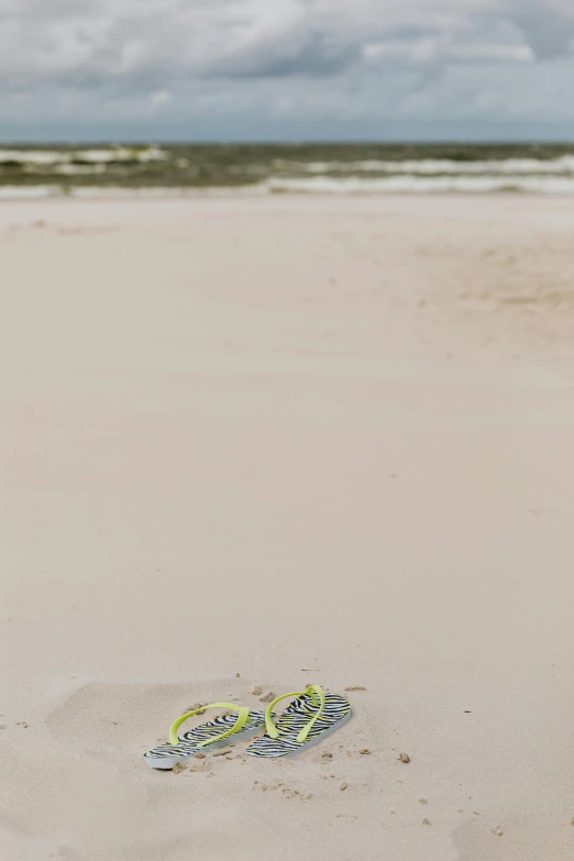 a pair of sandals sitting on top of a sandy beach, a picture, slight overcast, the emerald coast, mini model, litter