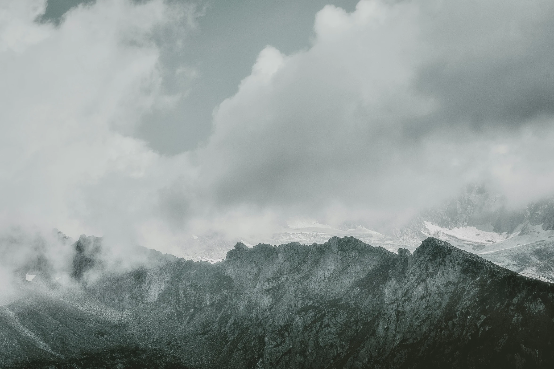 a person standing on top of a snow covered mountain, a black and white photo, unsplash contest winner, minimalism, grey clouds, 4 k hd wallpapear, seen from a distance, large rocky mountain