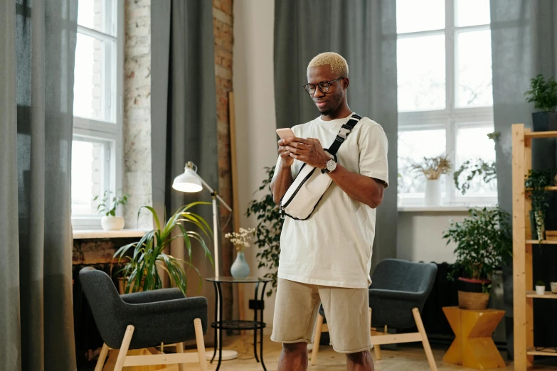 a man standing in a living room holding a camera, trending on pexels, visual art, carrying a saddle bag, checking her cell phone, black man, smart textiles