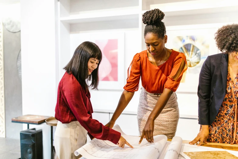 three women looking at blueprints on a table, pexels contest winner, 9 9 designs, wearing business casual dress, aida muluneh, woman holding another woman