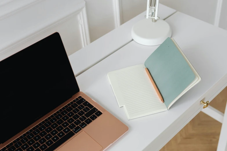 a laptop computer sitting on top of a white desk, by Carey Morris, trending on pexels, ivory and copper, teal paper, handcrafted, notebook