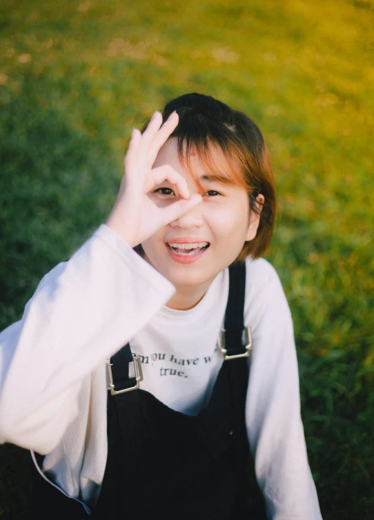 a woman sitting on top of a lush green field, a picture, by Tan Ting-pho, trending on unsplash, wan adorable korean face, with index finger, wearing a patch over one eye, waving and smiling