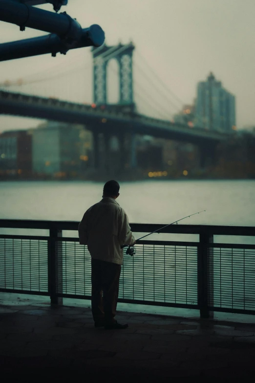 a man standing on a bridge with a fishing rod, inspired by Louis Stettner, pexels contest winner, tonalism, watching new york, photograph”