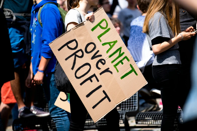 a protest sign in front of a crowd of people, by Julia Pishtar, the planet, promo image, high quality image, ecology