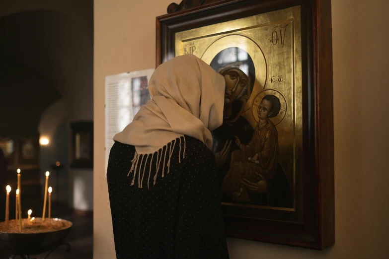 a woman standing in front of a painting with candles, a painting, by Emma Andijewska, pexels contest winner, qajar art, wearing white silk hood, in orthodox church, back view. nuri iyem, a wooden