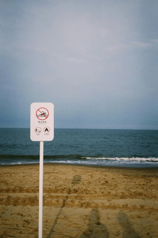 a white sign sitting on top of a sandy beach, a picture, by Aguri Uchida, unsplash, purism, water particulate, zezhou chen, stop sign, smoke :6