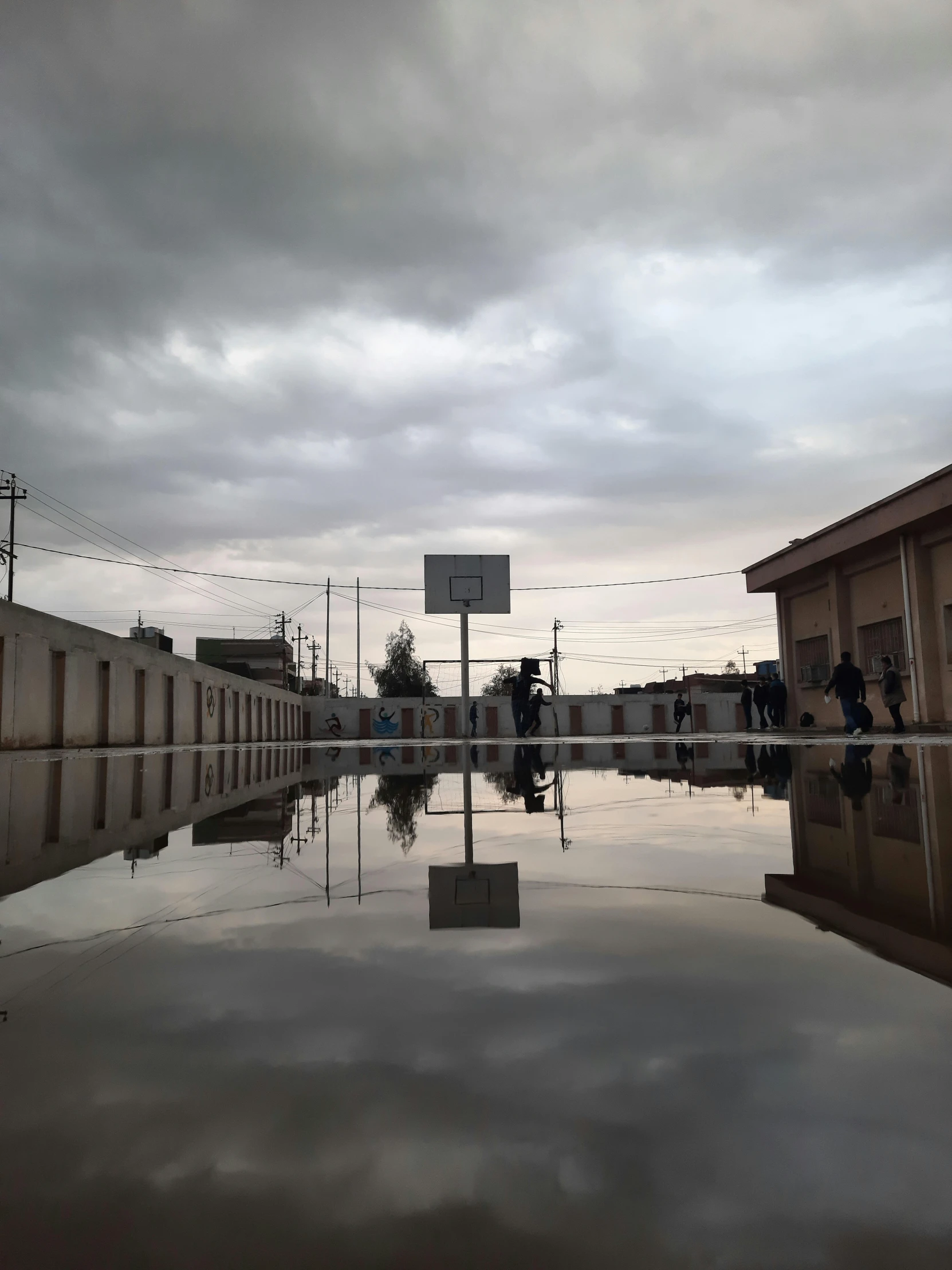 a puddle of water in front of a building, by Ibrahim Kodra, rojava, standing in a parking lot, high school, 2019 trending photo