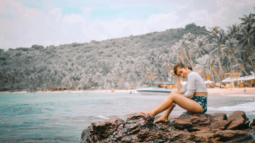 a woman sitting on top of a rock next to the ocean, pexels contest winner, tropical undertones, dressed in a top and shorts, avatar image, holiday