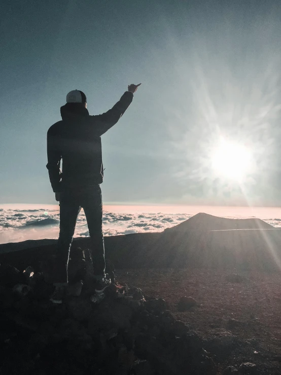 a man standing on top of a mountain pointing at the sun, by Niko Henrichon, pexels contest winner, big island, full body profile, trending on vsco, multiple stories