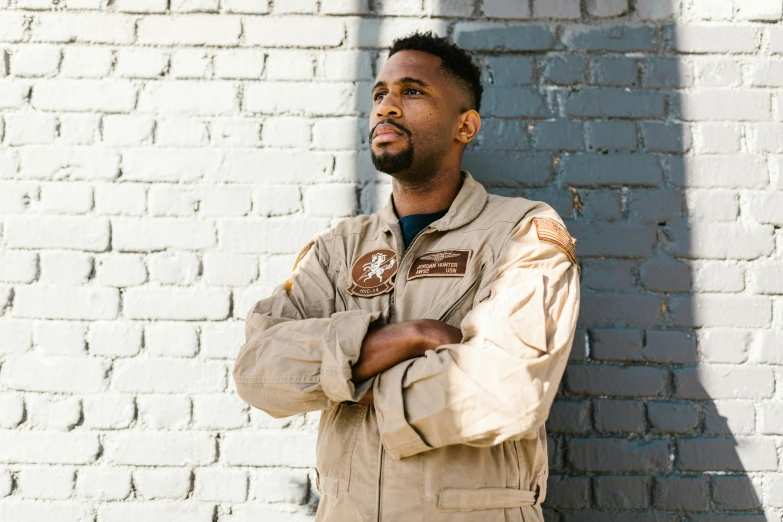 a man standing in front of a brick wall, wearing flight suit, aaron brooks, official store photo, profile image