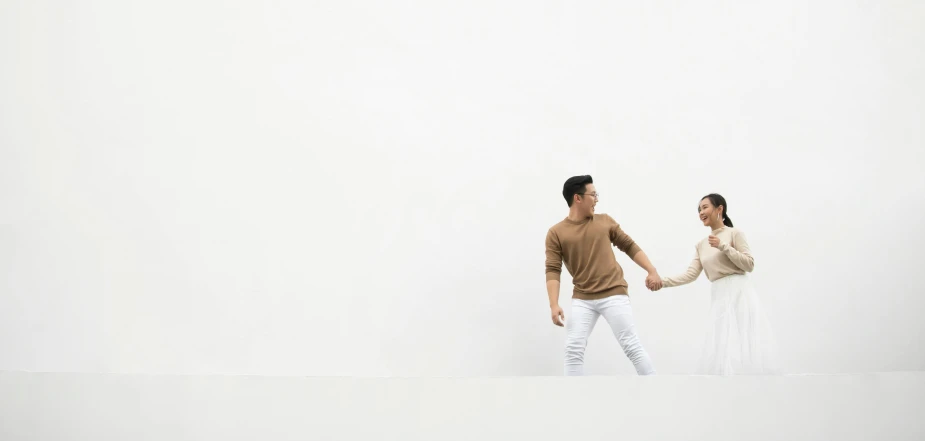 a man and a woman holding hands in a white room, an album cover, inspired by Fei Danxu, pexels contest winner, minimalism, he is wearing a brown sweater, playful pose of a dancer, man in white t - shirt, ross tan