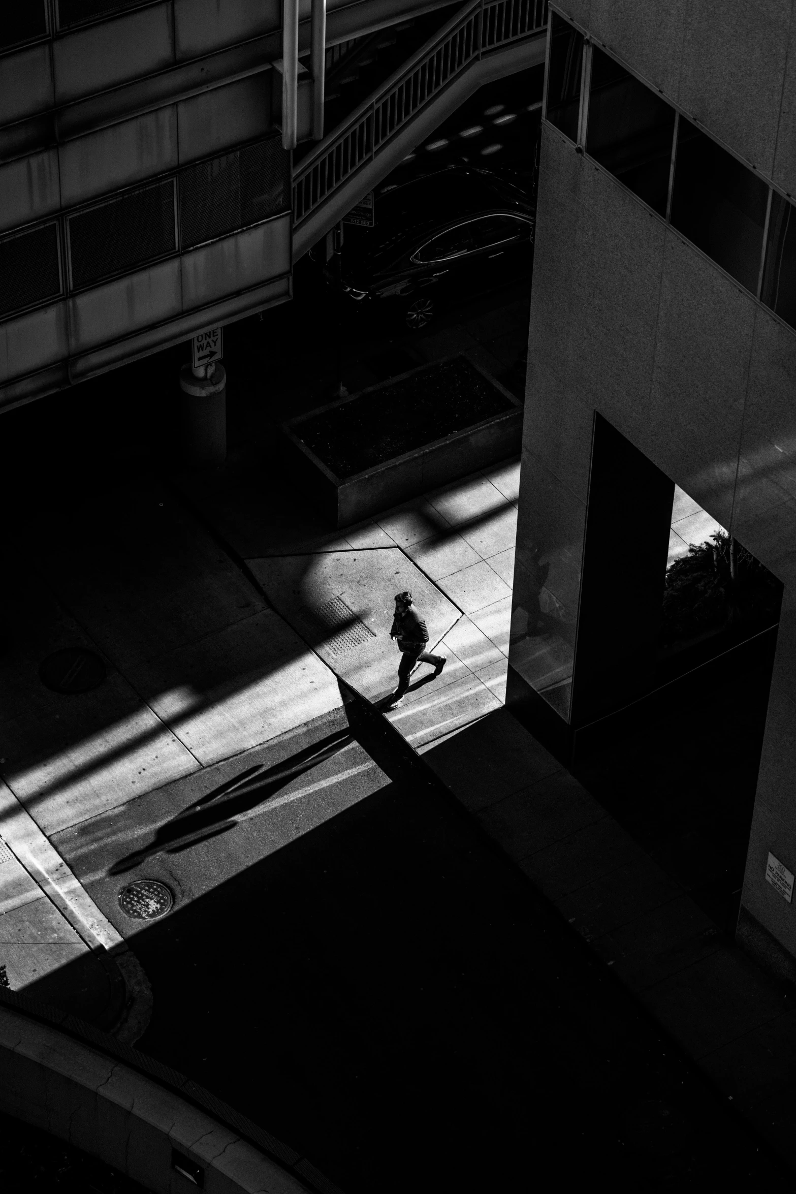 a black and white photo of a person walking down a street, unsplash contest winner, conceptual art, dramatic lighting from above, in a square, deep shadows and colors, photography of bill brauer