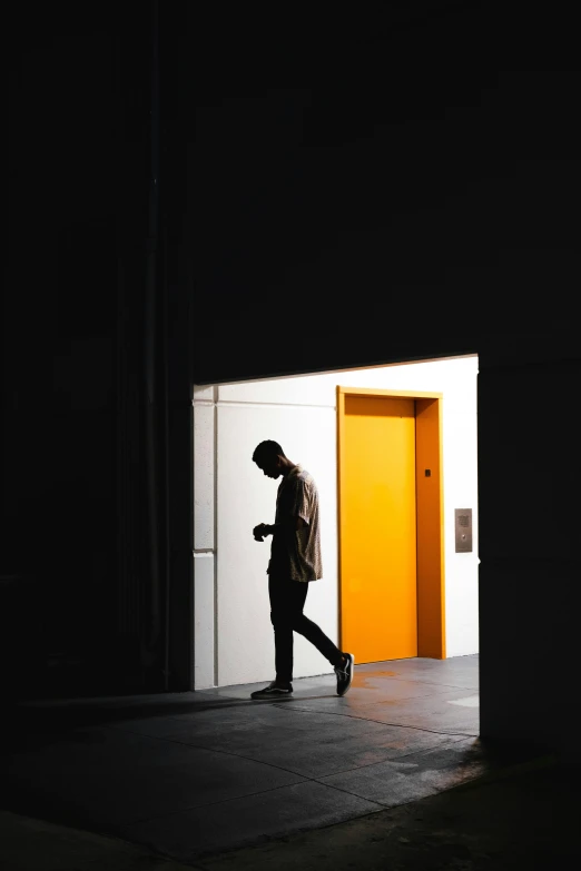 a man walking through an open door in a dark room, unsplash contest winner, postminimalism, gradient yellow, photo on iphone, people at work, black and orange