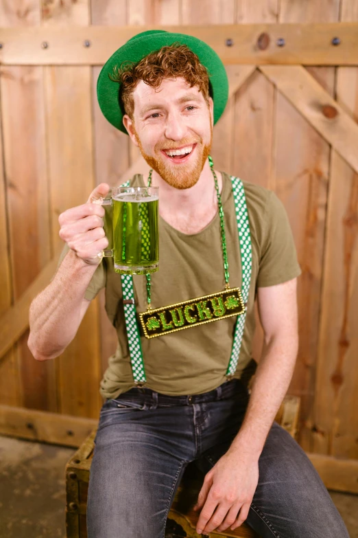 a man sitting on a stool holding a glass of beer, green halter top, four leaf clover, official store photo, suspenders