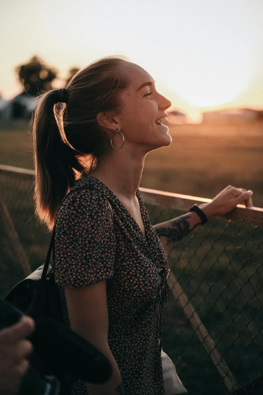 a woman standing in front of a fence at sunset, pexels contest winner, happening, smiling young woman, profile image, earing a shirt laughing, profile pic