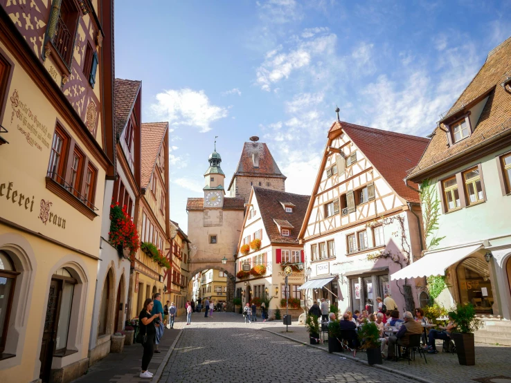 a group of people walking down a cobblestone street, by Julia Pishtar, pexels contest winner, renaissance, german renaissance architecture, white buildings with red roofs, bright sunny summer day, square