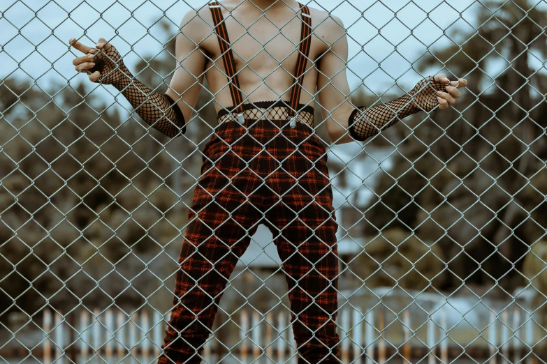 a man standing in front of a chain link fence, inspired by Elsa Bleda, trending on pexels, intricate leather suspenders, freddy krueger style, non binary model, 🦩🪐🐞👩🏻🦳