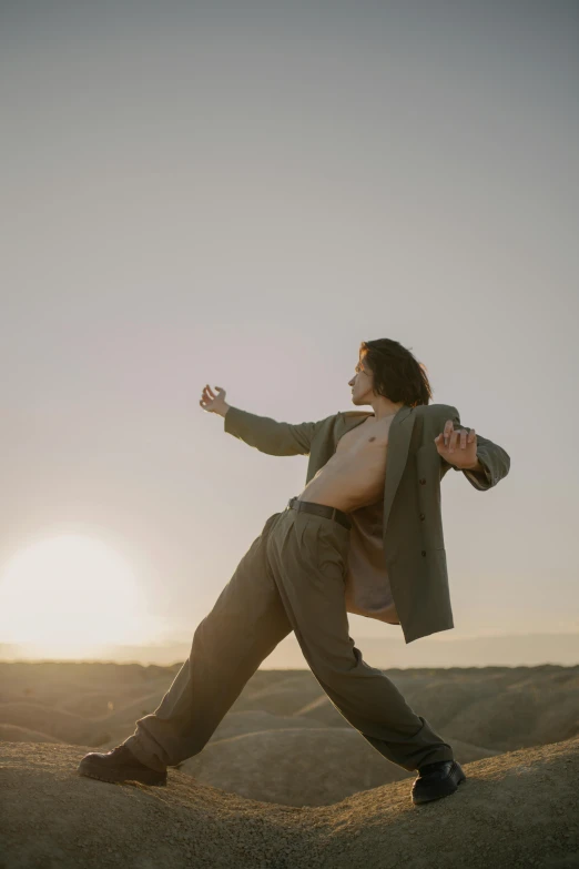 a woman standing on top of a hill with her arms outstretched, an album cover, unsplash, renaissance, finn wolfhard, karate pose, in desert, masculine pose